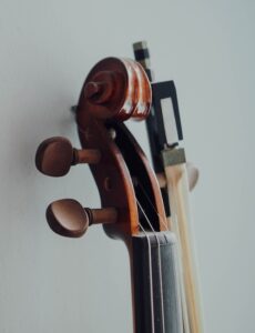 A full-color closeup image of a cello's neck and tuning keys alongside a cello's bow. 