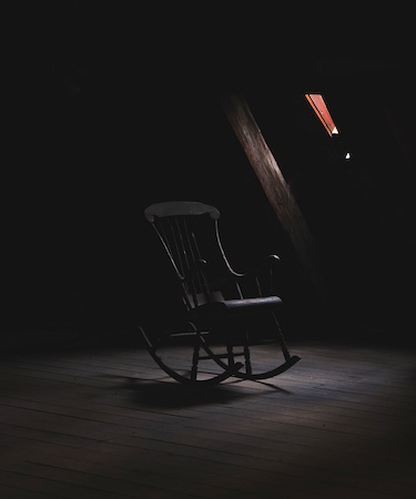 Rocking chair in a dark, attic room illuminated by a small notch in the ceiling. Used to illustrate Rickey Fayne's story "Spare the Rod."